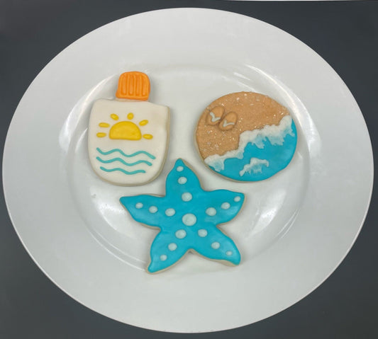 Decorative cookies shaped like a bottle, sand, and starfish on a white plate.